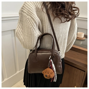 Detail of dark brown leather crossbody bag with teddy bear charm and textured branding