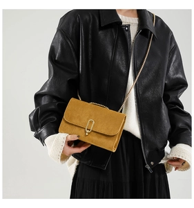 Detail of tan square crossbody bag with gold chain strap and vintage oval clasp on model