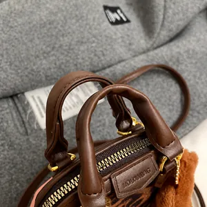 Detailed close-up of dark brown textured leather shell bag handle with plush pompom charm