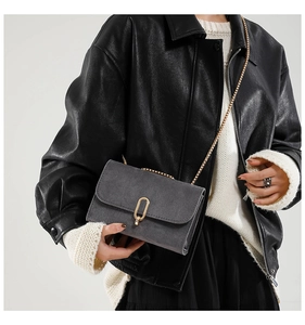 Detail of dark grey suede crossbody bag with gold buckle and chain on model
