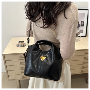 Detail of a black glossy bucket bag with golden triangle logo worn by a model