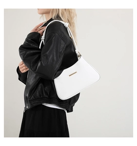 Detail of white shoulder bag with gold metal trim and woven knot strap on a model