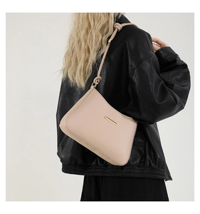 Detail of minimalist beige underarm bag with gold metal plate and knot strap on a model