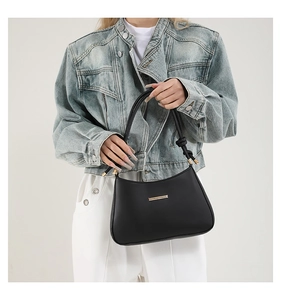 Close-up of minimalist black leather underarm bag with gold metal hardware and knot detail