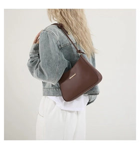 Brown faux leather shoulder bag with gold metal buckle detail shown on a model