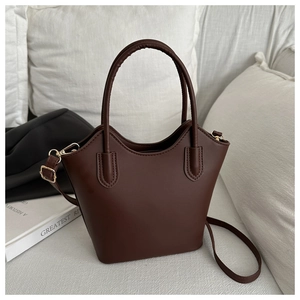 Detail view of dark brown bucket bag with curved top handle on white sofa