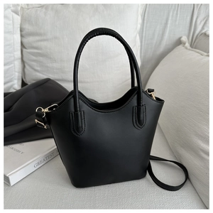 Detail of minimalist black matte leather bucket bag with gold hardware on white sofa