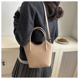Detail view of a beige matte leather bucket bag with an adjustable strap on a neutral background