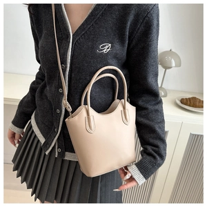 Close-up of beige minimalist bucket bag with round handles and long strap in interior setting