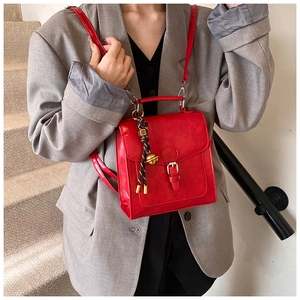 Detail of red leather crossbody bag featuring a golden metal buckle and woven knot charm