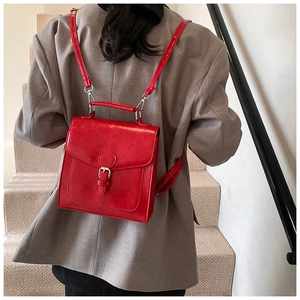 Detail view of a vibrant red leather backpack with silver buckle on a stylish model