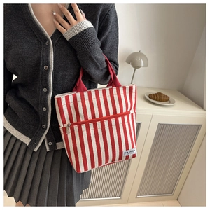 Detail view of red and white striped canvas tote bag with front zipper and fashion label