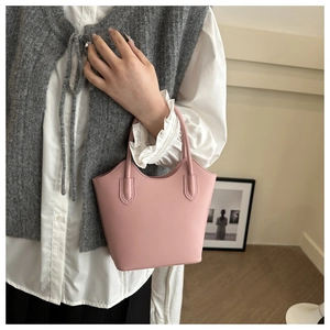 Detail view of pink leather bucket bag showing cylindrical handles and minimalist texture