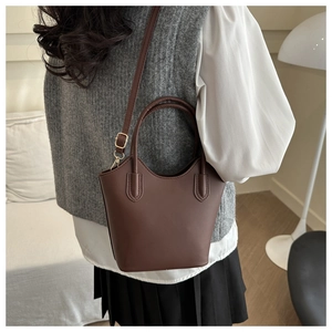 Detail of chocolate brown bucket bag with gold buckles worn by model in a cozy interior