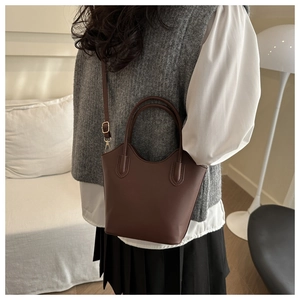 Brown bucket bag styled with a gray vest and white shirt in a cozy indoor setting
