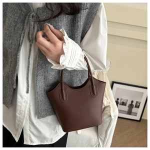 Deep brown leather bucket bag shown held by a model in an elegant lifestyle setting