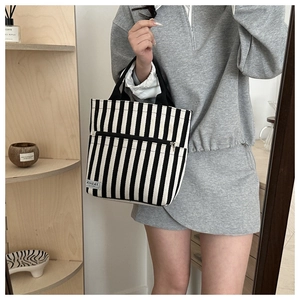 Detail of striped canvas tote bag showing black handles and functional front zipper pocket