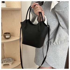 Detail of black bucket bag with wavy rim, top handles, and adjustable shoulder strap