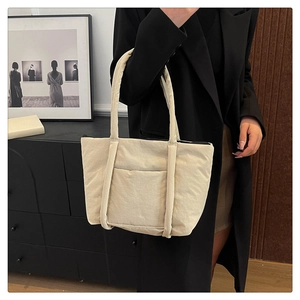 Detailed view of beige padded tote bag with large front pocket held by model in black suit