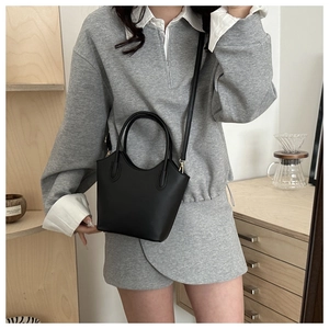 Detail of minimalist black bucket bag showing matte leather texture and styling on model