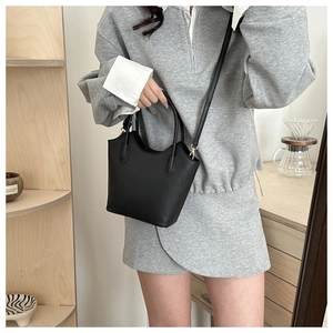 Detailed view of a black leather bucket bag worn as a crossbody with adjustable strap