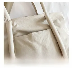 Detail of beige tote bag featuring a practical front pocket and reinforced tubular handle