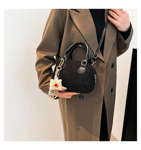 Detail of black bowling shoulder bag with a cute bear pendant on a brown trench coat