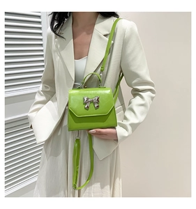 Detail of green PU leather crossbody bag with silver metal bow and thin strap