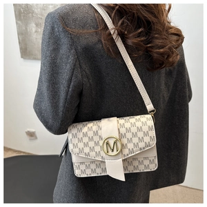 Detail of minimalist cream crossbody bag with grey M monogram and gold logo buckle