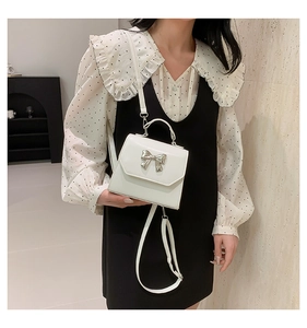 White mini square bag featuring a 3D silver bow and adjustable crossbody strap detail