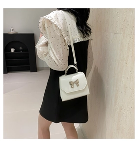 Close-up of a white patent leather handbag featuring a decorative gold bow buckle detail