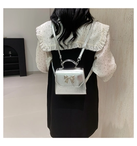 Detail of silver metallic mini backpack featuring a bow accent on a model's back