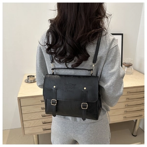 Model wearing a black faux leather briefcase backpack with gold buckles and lucky stamp