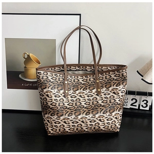 Détail du sac cabas léopard avec anses marron et rivets dorés sur un bureau