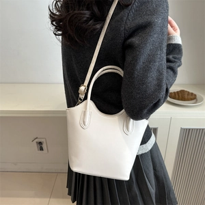 Minimalist white leather bucket bag for women showing versatile top handle and shoulder strap