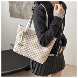 Detailed view of beige monogram tote bag with gold M pendant and slim shoulder straps
