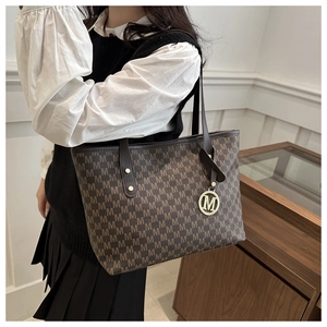 Detail of dark brown tote bag featuring M-pattern monogram and gold letter charm