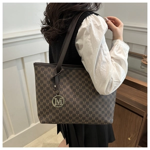 Detail of dark brown tote bag featuring all-over M monogram and gold metal charm
