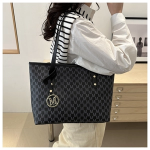 Detail of black tote bag with M-pattern print and golden metal letter charm
