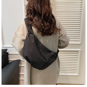 Rear view of a model wearing a large black nylon crescent crossbody bag in a minimalist style