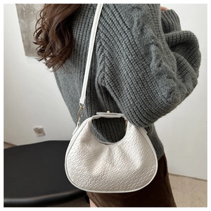 Detail of white woven textured crescent bag with gold buckles on grey sweater background
