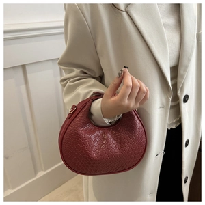 Macro shot of burgundy woven leather texture and elegant gold hardware on crescent bag