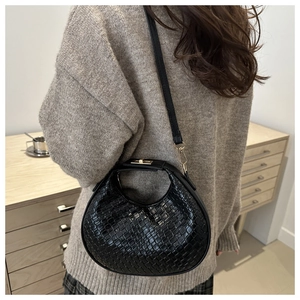 Detail of black crescent crossbody bag with crocodile texture and gold clasp on shoulder