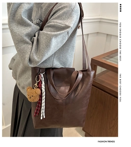 Detail of dark brown tote bag with plush bear charm and fashion text embossing