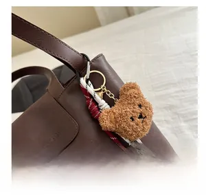 Detail of cute brown teddy bear plush pendant with gold hardware on a leather handbag