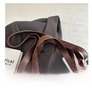 Detail of a brown leather tote bag with reinforced handles and a soft pompom charm