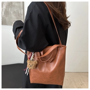 Brown faux leather tote bag with plush bear charm worn by a model in a side view