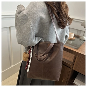 Shoulder view of a brown leather tote bag with a fashion logo and cute bear charm
