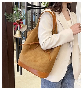Brown suede tote bag with leather bow decoration shown on shoulder by female model