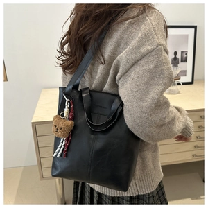 Detail of black tote bag with embossed fashion lettering and plush bear charm decoration